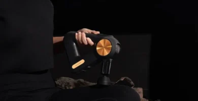 PISTOLA DE MASAJE THERAGUN COLOR NEGRO Y DORADO SIENDO UTILIZADA PÒR UNA MUJER VESTIDA DE NEGRO